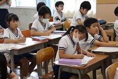 学校の教室で机に座って物を書いている体操服姿の児童たちの写真