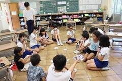 学校の教室で児童たちが床に座りながら円になってトランプをしている写真