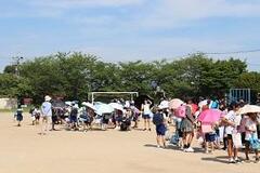校庭でたくさんの人が日傘を差しながら歩いている写真