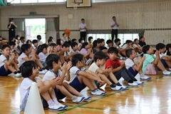 体育館の床に並んで体育座りをしている子どもたちの写真