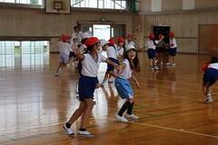 学校の体育館で体操服と紅白帽姿の子供たちが運動をしている写真