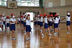 学校の体育館で体操服と紅白帽姿の子供たち歩き回っている写真