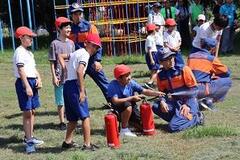 消防服を着た男性と1人の子どもが消火器から水を出しており、それを紅白帽を被った子どもたちが見ている写真