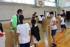 学校の体育館で子どもたちが段ボールを持って四角の形に設置しようとしている写真