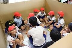 段ボールで四角形の形に仕切られたスペースの中に紅白帽の子どもたちが座りながら入っている写真