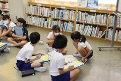 学校の図書館で子供たちが床に座ってファイルを抱えながら話し合いをしている写真