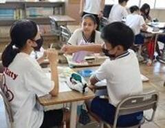 学校の教室で机を繋げた3人の子供たちがお互いを見ながら話をしている写真