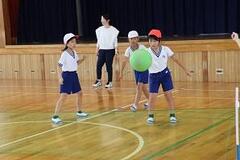 体育館で紅白帽と体操服姿の子どもたちがボールで遊んでいる写真