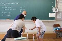 学校の教室の黒板の前で男の子と大人2人がお互いに向き合って下を向いている写真