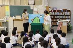 室内で床に座った子どもたちの前で女性2人が大きな絵本を見せている写真