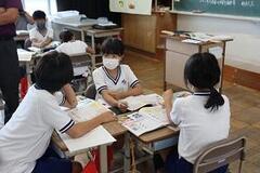 学校の教室で3人の子供たちが机を合わせて本を広げながら話合いをしている写真