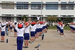 学校の校庭で体操服姿の子供たちが整列しながら体操をしている写真