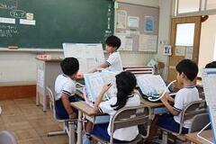 教壇前で大きな紙を持った児童と鍵盤ハーモニカを演奏している児童たちの写真