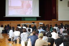 スクリーンに映し出された映像を見ている6年生の生徒たちの写真