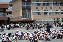 引き渡し訓練の写真。大勢の生徒と保護者たちが学校の校庭にいる。