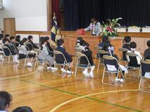 体育館で新1年生たちが座り、教壇で先生が話をしている写真