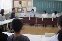 幾つかの長机を合わせて複数の児童や大人達が座っている写真