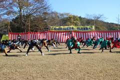沢山の児童達が足を広げ腰を低くしており、その後ろに紅白幕が掛かっている写真