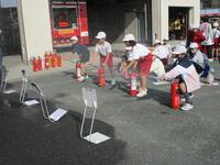 児童達が横一列に並んで、消化器を手に持ってパネルのようなものをめがけて放水を行っている写真