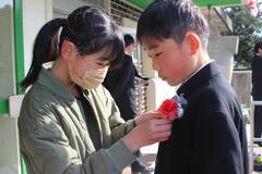1人の女子児童が男子児童の胸元にコサージュのようなものを付けている写真