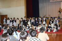 ステージ前に並んだ児童達が前後2列になって並んでいて、前列の児童は座って、後ろの児童は立っている写真