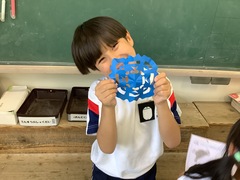 教室の黒板の近くで出来上がった切り絵を見せる1人の児童の写真