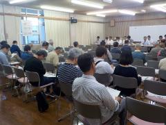 椅子に座って説明を聞いている人たちの写真