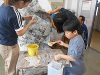 貼りつけられた新聞紙の表面を白く塗っている児童の写真
