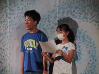 渦巻の幕を背にして朗読を行う生徒代表の写真