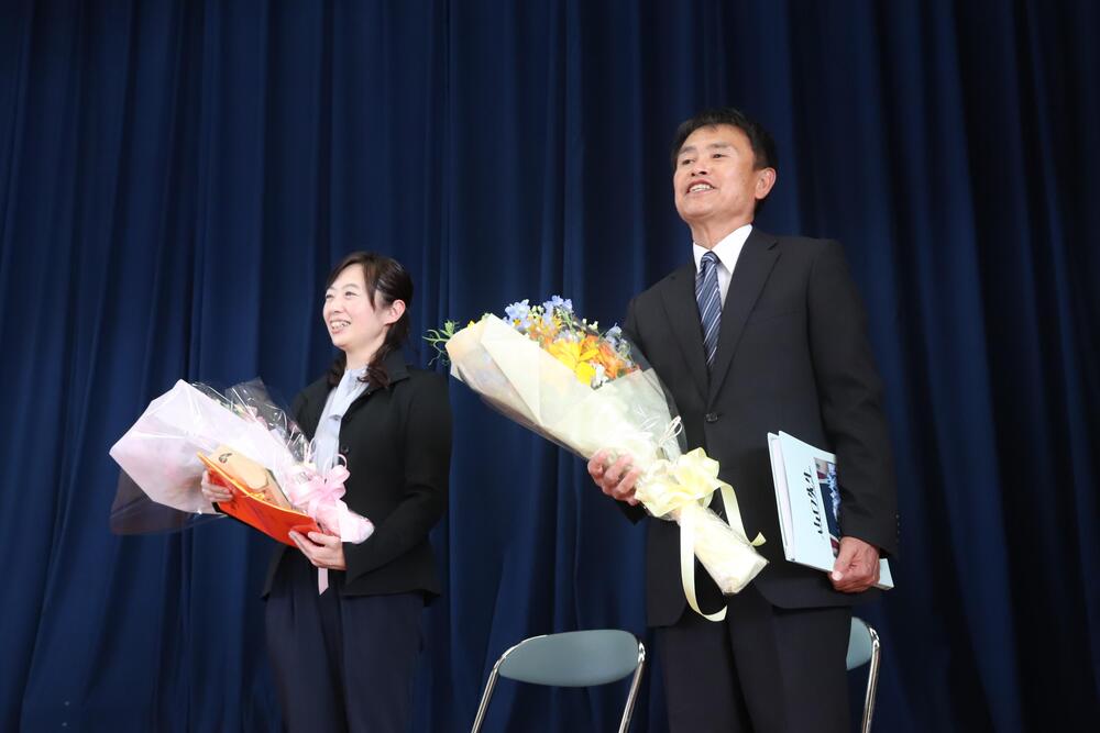 紺色の幕の前に花束をもって立つ山口先生と村松先生の写真
