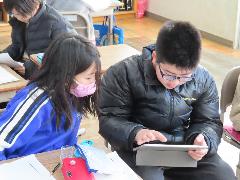 低学年の子にタブレット端末を使ってアドバイスする高学年の子