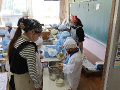 給食ボランティアの方の見守る中、食材を盛り付ける子どもたち