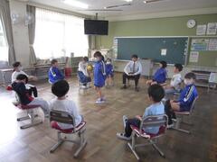 立っている児童を囲うように置かれた椅子にそれぞれ児童たちが座っている写真