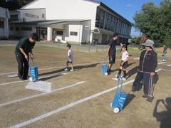 校庭に白線を引く大人たちとその周りを歩く子供の写真