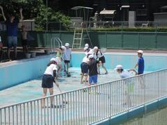小さいプールをデッキブラシなどで掃除をしている児童たちの写真
