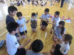 体育館に膝立ちで円になって一緒に1つの輪を持っている子供たちの写真