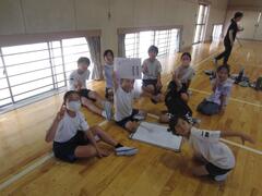 体育館の床に置かれたホワイトボードの周辺に集まりこちらにポーズを取る子供たちの写真