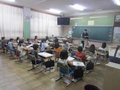 教卓に立つ大人の話を席に着いて聞く子供たちの写真