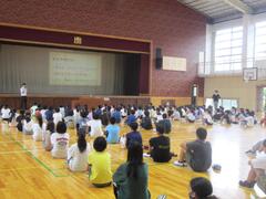 体育館の床に列になって体育座りする子供たちの写真