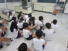 室内の床に座った子供たちの内、真ん中の子をのぞき込んでいる白衣姿の女性の写真