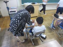 紺に水玉模様の入った服を着た大人が席に着いている子供に指導している写真