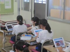 タブレットが置かれた机で勉強をする子供たちの写真