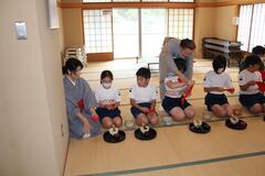 和室に横一列に正座して座ってお茶のお作法を着物姿の女性に学んでいる子供たちの写真