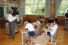 白髪の大人が見せている資料を席に着いて見ている子供たちの写真