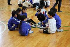 体育館の床に円になって座る数人の子供たちの写真
