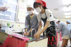 エプロンと三角巾を着けた人がが手を洗っている写真