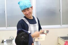 エプロンと三角巾を着けた男の子が子供と話している写真