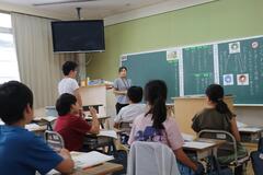 教室の席に着く子供たちの中で、1人の子供が立っている写真