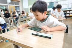 削られていない鉛筆を机の上に立てようとしている男の子の写真