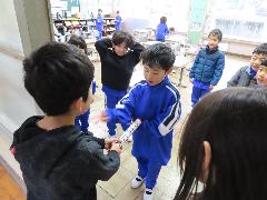 3年生の子どもが1年生の子どもにあいさつバトンを受け渡す様子